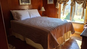Un dormitorio con una cama grande, paredes de madera, una mesita de noche con lámpara y cuadros enmarcados en la pared.