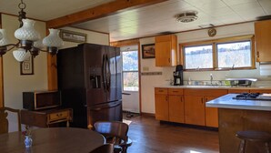 Una cocina con armarios de madera, un refrigerador, una cafetera y una mesa de comedor con sillas.