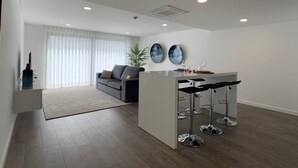 Una sala de estar moderna con un sofá, una mesa baja y una zona de comedor con taburetes de bar.