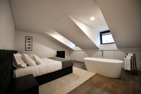 A modern bedroom with a large bed, a built-in bathtub, and a skylight.