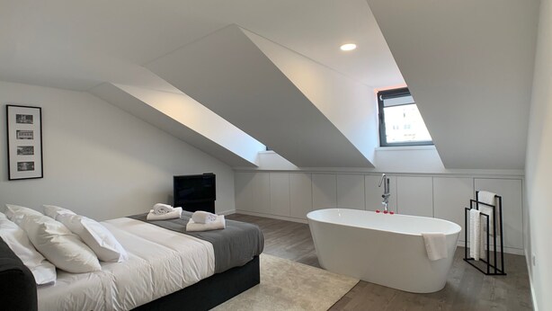 Un dormitorio moderno con una cama grande, un televisor de pantalla plana, un tragaluz y una bañera independiente.
