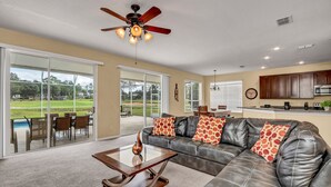 A spacious living room with a leather sofa, a glass coffee table, and a ceiling fan. - Family Villa With Pool and Golf, 20 Mins To Disney (Davenport)