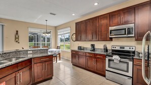 A spacious kitchen with granite countertops, stainless steel appliances, and wooden cabinets. - Family Villa With Pool and Golf, 20 Mins To Disney (Davenport)