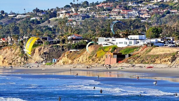 A coastal beach with houses on a hillside, a sandy shore, and people surfing. - FAST WiFi, NEW 1 Block to Beach Sparkling Clean A/C BBQ Parking (San Diego)