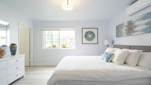 A bedroom with a large bed, a dresser, a window, and a wall-mounted air conditioner. - FAST WiFi, NEW 1 Block to Beach Sparkling Clean A/C BBQ Parking (San Diego)
