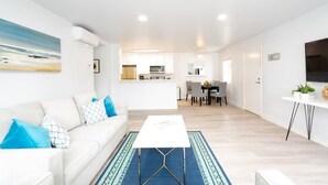 A modern living room with a white sofa, a coffee table, and a dining area in the background. - FAST WiFi, NEW 1 Block to Beach Sparkling Clean A/C BBQ Parking (San Diego)