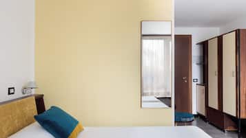 Une chambre d’hôtel avec un lit, une table de chevet, une lampe, une armoire et un miroir au mur.