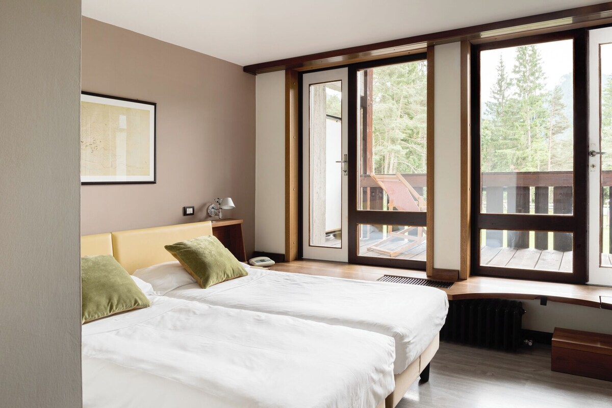 A bedroom with two beds, a desk, and large windows overlooking a deck.
