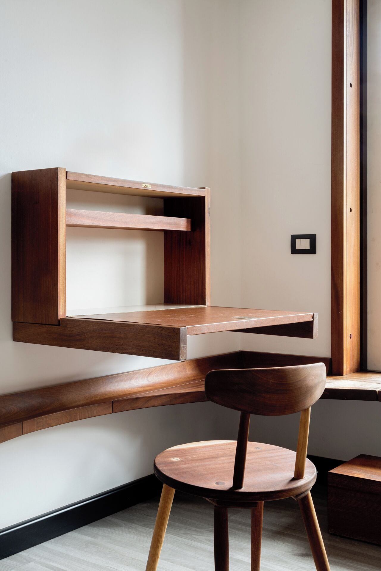 A minimalist room with a wooden desk and chair, a wall-mounted shelf, and a small wooden cabinet.