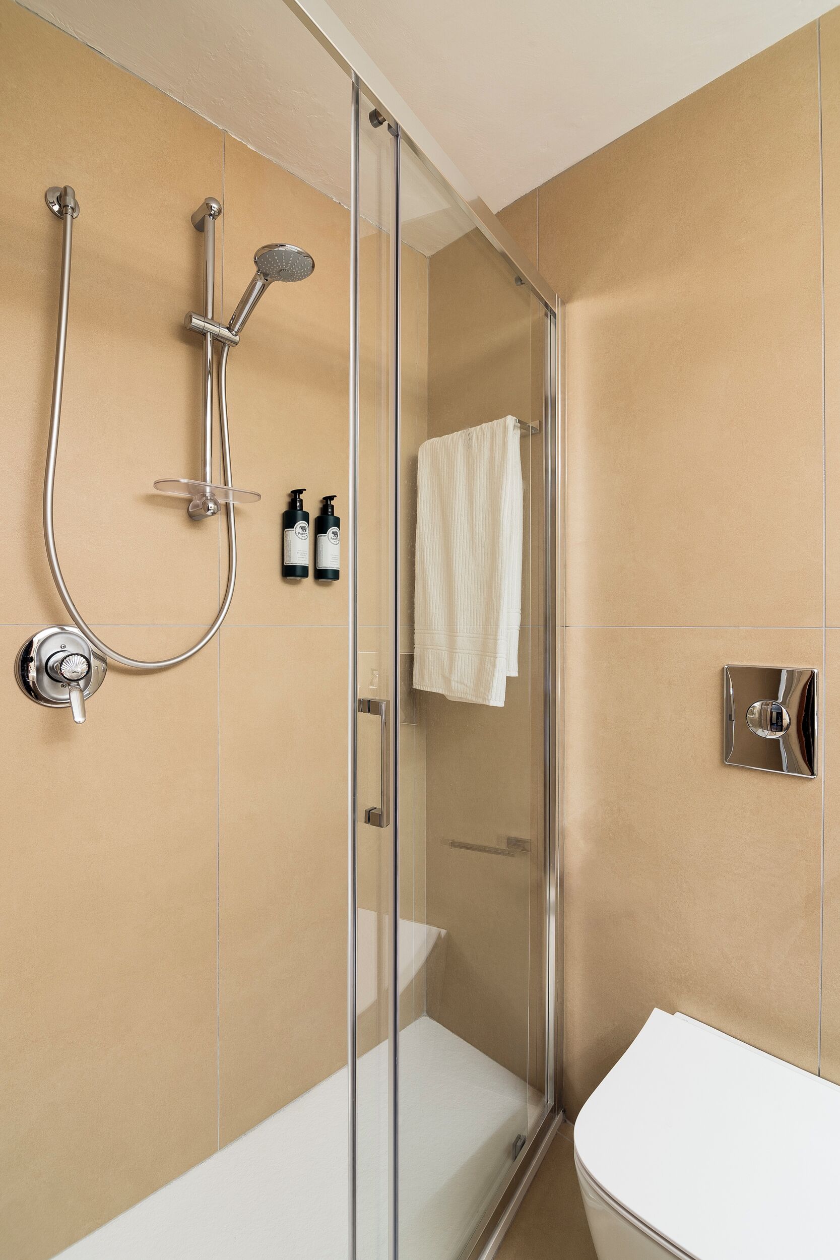 Un baño moderno con ducha de vidrio, inodoro blanco y una toalla colgada en la pared.