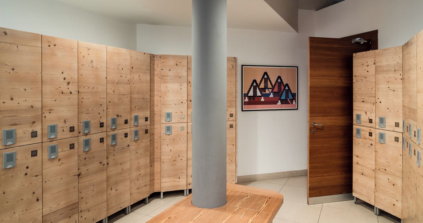 A row of wooden lockers with numbered compartments, a gray pillar, and a door with a wooden panel.