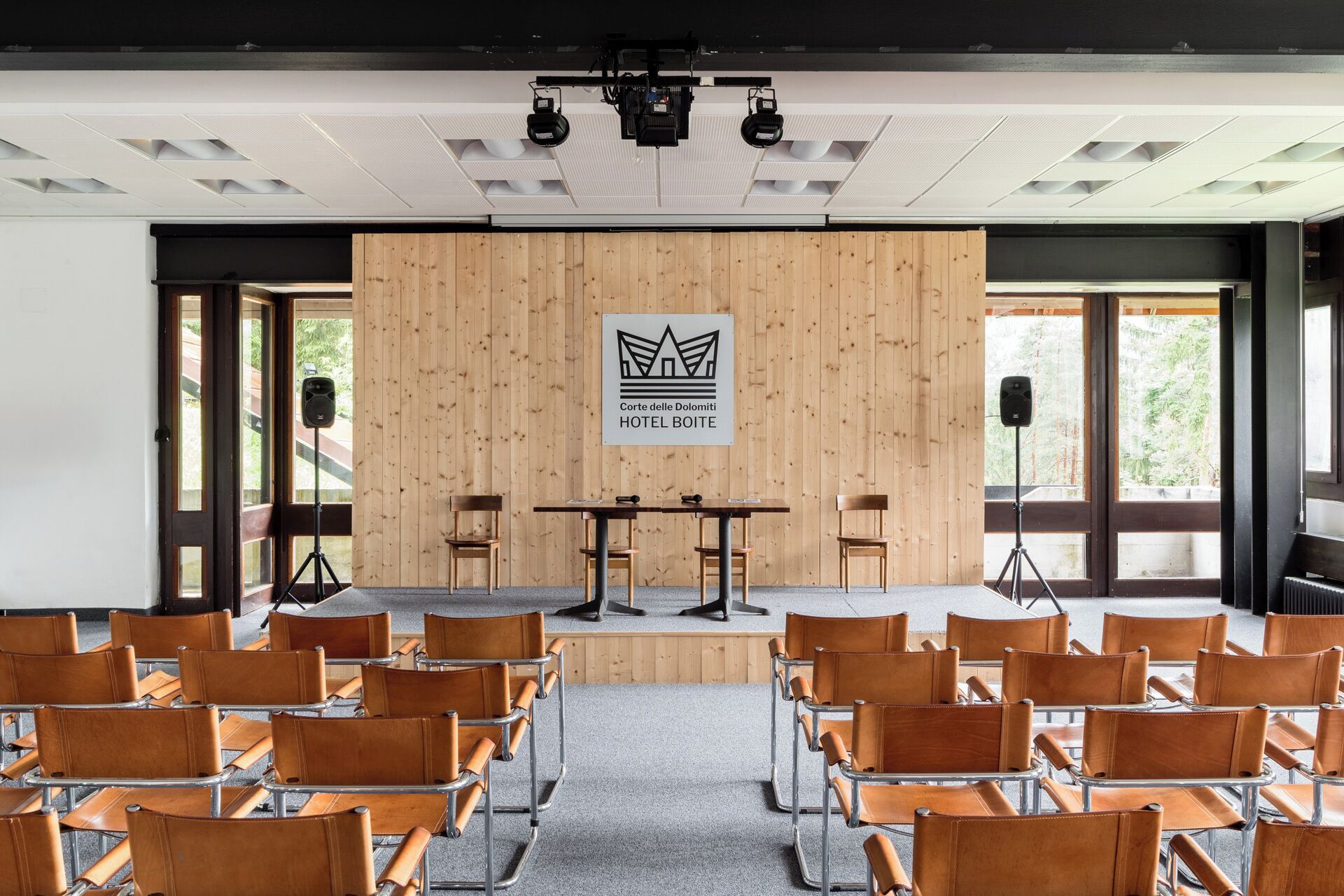Un salón de conferencias con un panel de madera, un escenario con un atril y filas de sillones de cuero.