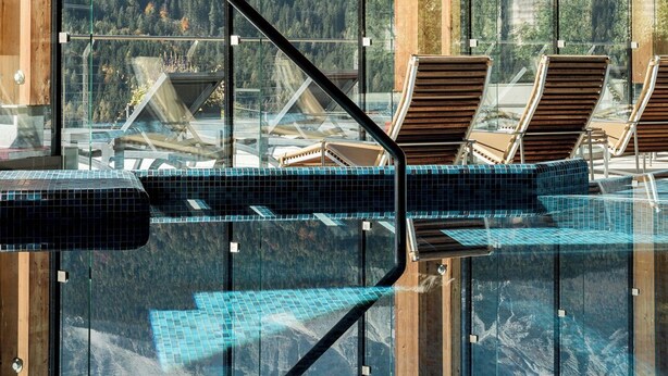 A glass-enclosed infinity pool with wooden deck chairs, reflecting a mountainous landscape. - Hotel Boite (Borca di Cadore)