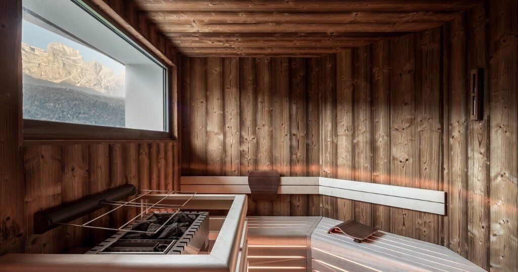 A wooden cabin with a built-in wood stove, a window overlooking mountains, and a bench by the window.