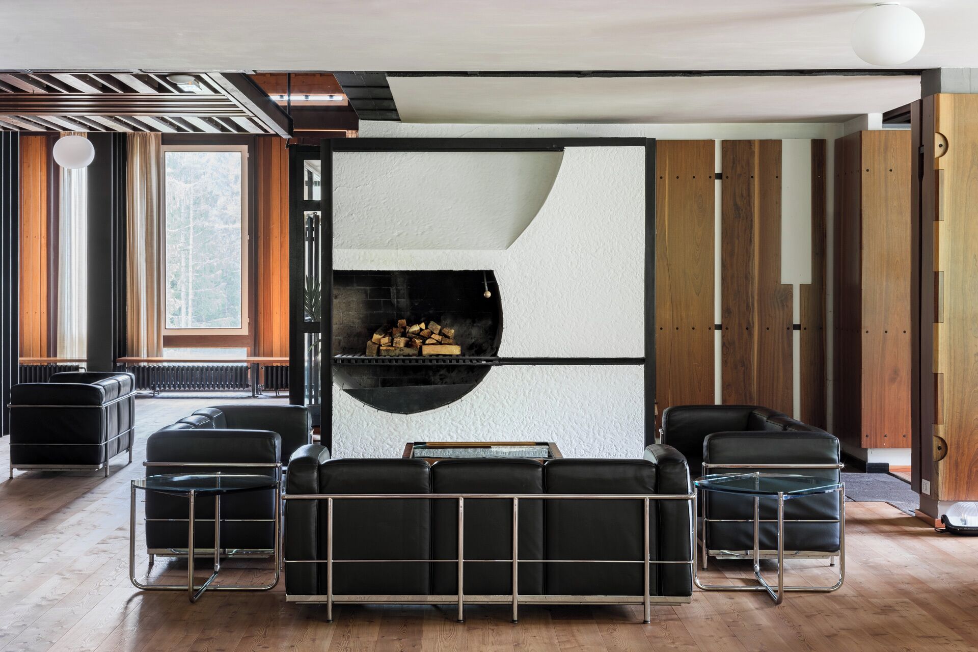 A modern living room with a built-in fireplace, black leather sofas, and a glass coffee table.