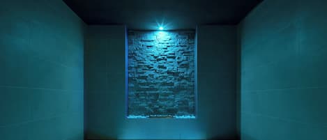 A room with a stone wall feature and a light source above it.