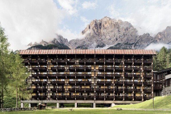 Un hotel a più piani con balconi, con le montagne sullo sfondo.