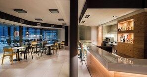 Un ristorante moderno con area bar, caratterizzato da diverse tipologie di posti a sedere e vista sulla città attraverso ampie finestre.