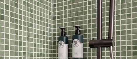 Ein Badezimmer mit grünen Mosaikfliesen, einem Duschkopf und zwei Flaschen Parco Shampoo.