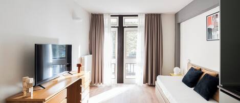 Quarto de hotel moderno com televisão de tela plana, cômoda de madeira e uma cama com travesseiros escuros.