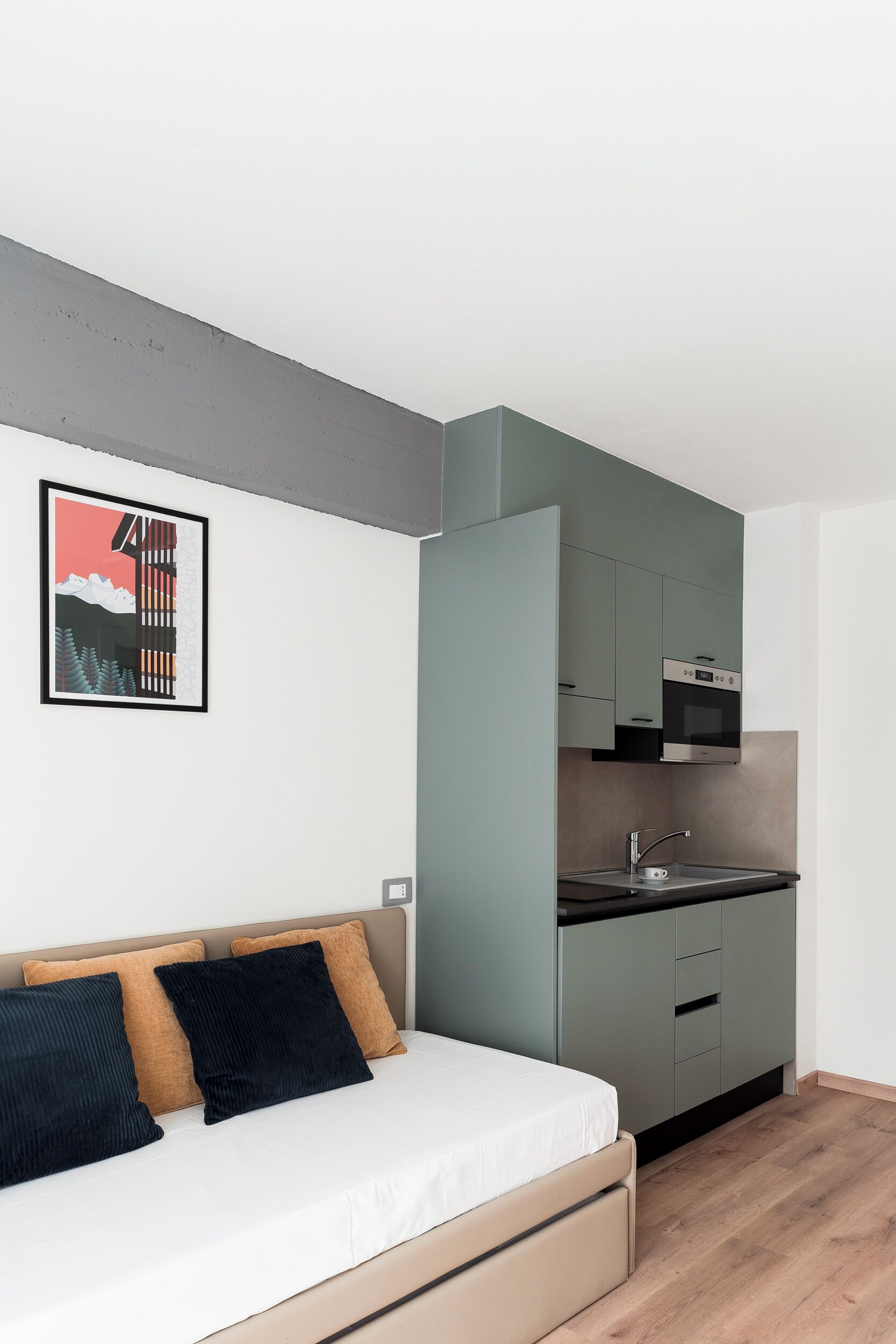 Eine moderne Küche mit grauen Schränken, einer Edelstahl-Spüle und einer Mikrowelle. Ein Bett mit weißer Matratze und zwei Kissen, eines schwarz und eines braun.