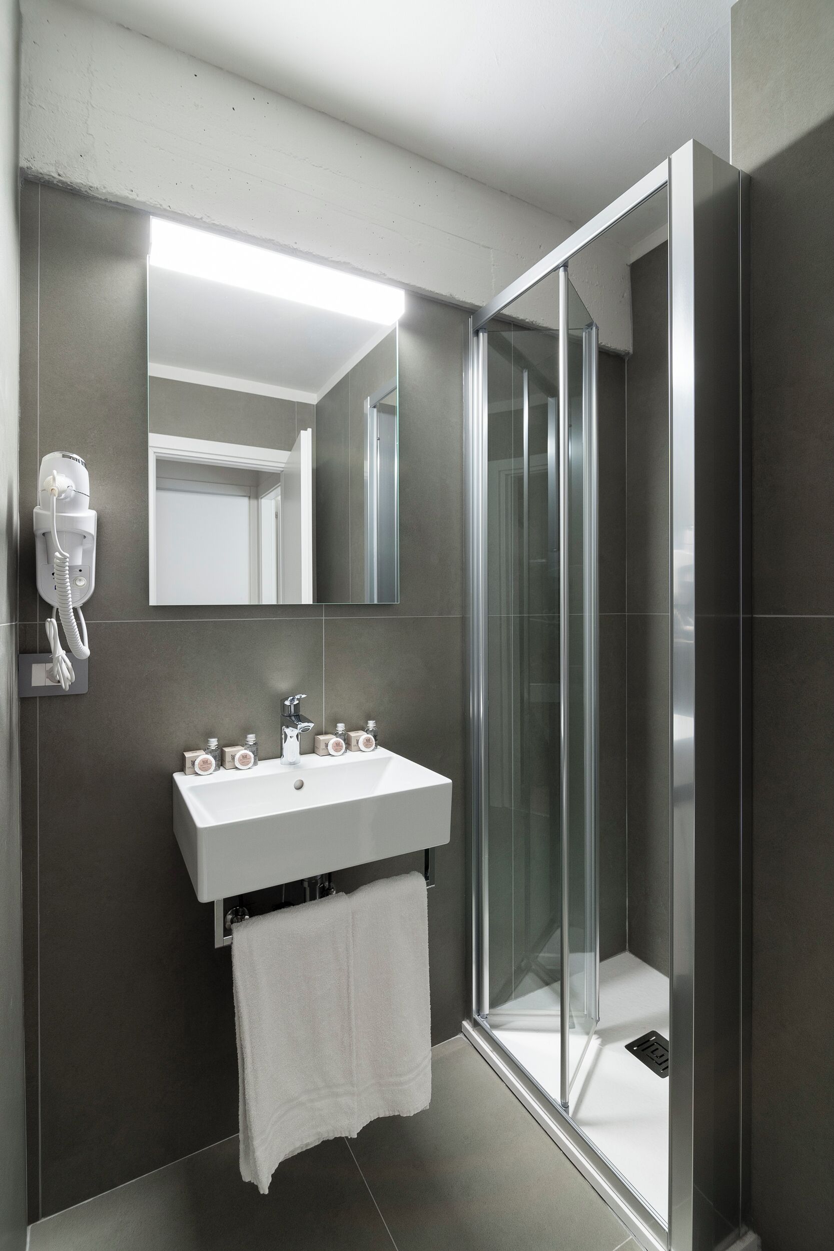 Un baño moderno con un lavabo blanco, una cabina de ducha con mampara de vidrio y un espejo sobre el lavabo.
