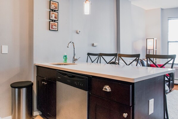 A compact kitchen with a dishwasher, a sink, and a small trash bin. There are three chairs and a dining table. - Lovely 2BR apt. by Wooster Sq.- great location! (New Haven)