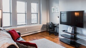 Un salon moderne avec un canapé en cuir, un tapis blanc, un bureau avec une chaise et un téléviseur à écran plat posé sur un meuble.