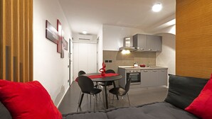 Un espacio habitable compacto con comedor, kitchenette y sofá con cojines rojos y grises.