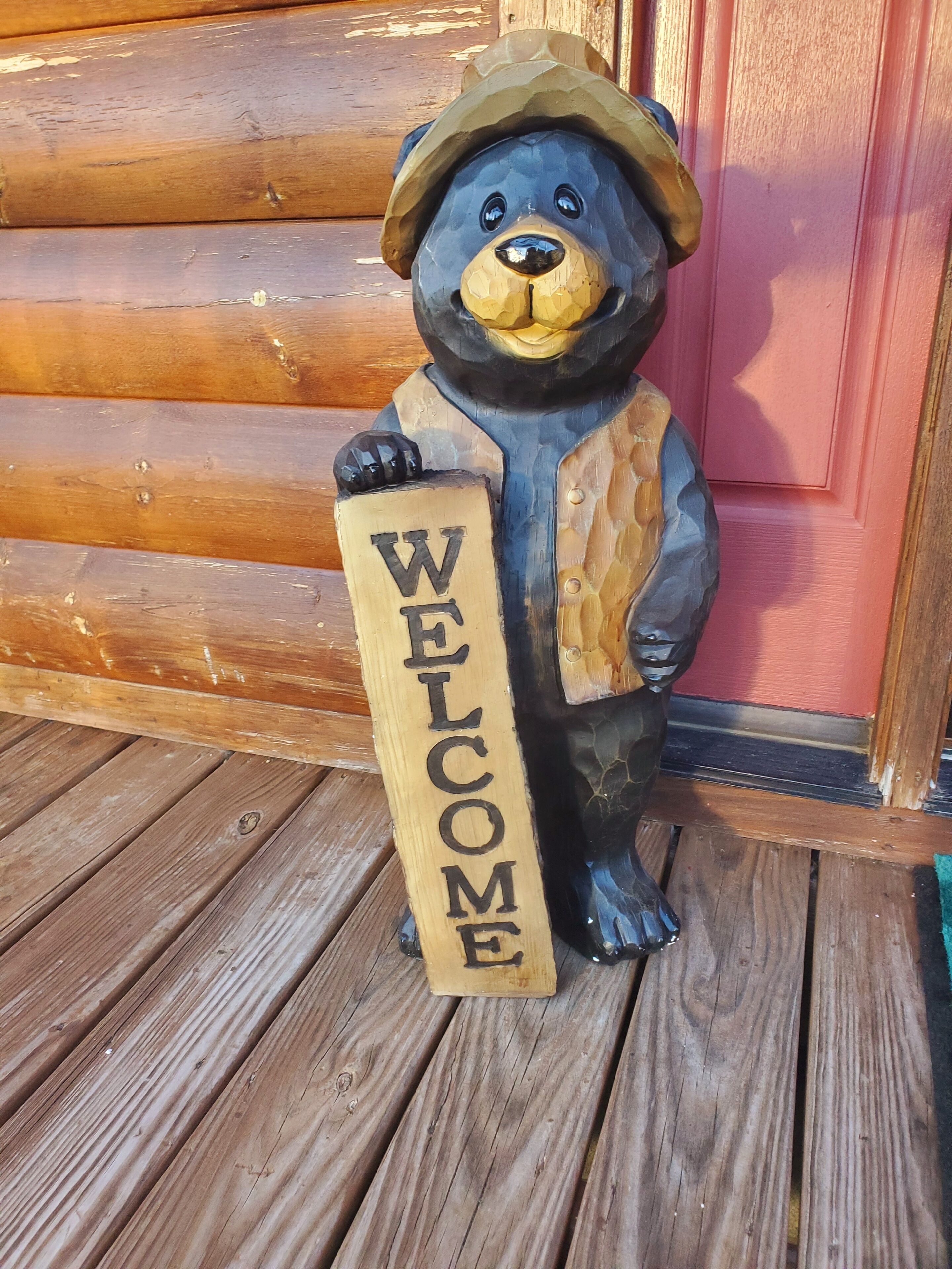 Een houten beeld van een beer dat een bord vasthoudt met daarop 'WELCOME'.