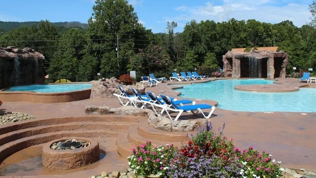 A pool area with lounge chairs, a fire pit, and a waterfall feature. - Easy Drive Resort Cabin w/ Hot Tub, Mtn View, and Resort Pool Near National Park (Gatlinburg)