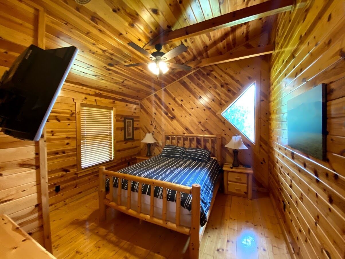 A cozy log cabin bedroom with a bed, two bedside tables, a ceiling fan, and a window.