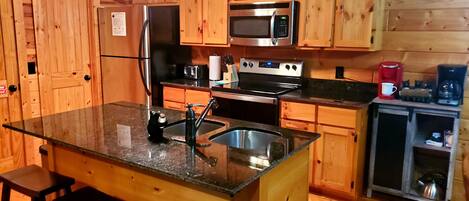 Cocina tipo cabaña de madera con una isla central, electrodomésticos de acero inoxidable y armarios de madera.