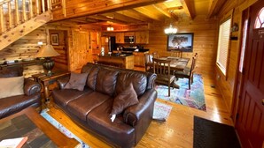 A wooden cabin interior with a leather sofa, dining table, chairs, and a staircase. - Easy Drive Resort Cabin w/ Hot Tub, Mtn View, and Resort Pool Near National Park (Gatlinburg)