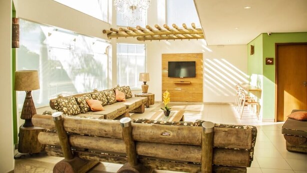 A modern living room with a large sofa, a TV mounted on a wooden wall, and a chandelier. - Meu Hotel Garça (Garca)