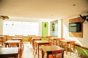 Un comedor con mesas y sillas de madera, un ventanal grande, una pared de acento verde y un televisor montado.