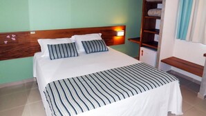 A neatly made bed with a striped bedspread and pillows, a bedside lamp, and a wooden headboard. - Meu Hotel Garça (Garca)