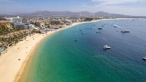 An aerial view of a coastal city with a wide sandy beach, numerous boats in the water, and a dense urban area with buildings in the background. - 180 degree unobstructed ocean view - building 3, 3 Bedrooms, can also rent as 2 (Cabo San Lucas,)