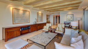 Een ruime woonkamer met een hoge plafond, houten balken, een grote bank, een salontafel en een zithoek met stoelen.