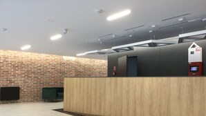 A reception area with a wooden reception desk, a brick wall, and a modern ceiling with recessed lighting. - Apartment Go at Rakowicka street  located just few minutes walk from city center (Kraków)