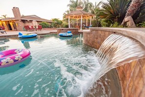 A pool area with a waterfall feature, inflatable rings, and a gazebo.