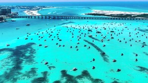 Vista aérea de una zona costera con numerosos barcos, un puente y una costa distante con edificios.