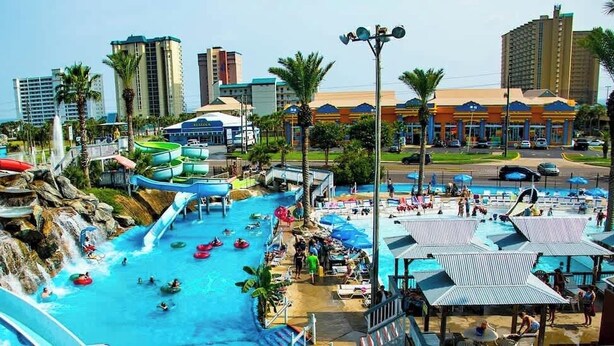 Parque acuático con múltiples toboganes y piscinas, rodeado de palmeras y edificios.