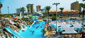 Parque acuático con múltiples toboganes y piscinas, rodeado de palmeras y edificios.
