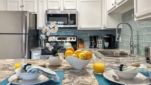Una cocina con gabinetes blancos, un refrigerador de acero inoxidable, un microondas y una cafetera.