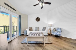 A bedroom with a bed, a ceiling fan, a wall clock, a chessboard, and a view of the outdoors.
