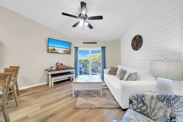 A living room with a white sofa, a coffee table, a television, and a ceiling fan.