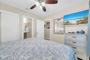 A bedroom with a bed, a dresser, a ceiling fan, and a TV on the wall.