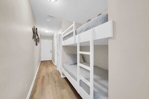 Un pasillo estrecho con literas, suelo de madera y una puerta blanca al final.