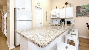 Una cocina con armarios blancos, encimera de granito, refrigerador, microondas y cafetera.
